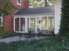 an enclosed patio with table and chairs in front of a brick building surrounded by greenery