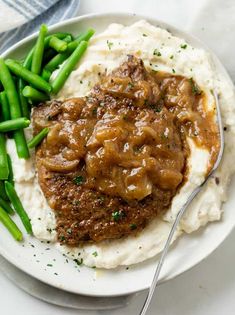 a white plate topped with mashed potatoes covered in gravy and green beans