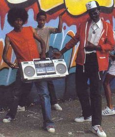 three young men standing in front of a graffiti covered wall holding an old radio and boombox