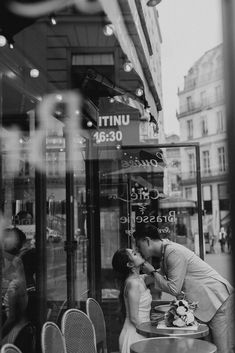 a man and woman kissing in front of a restaurant window with people sitting at tables