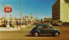 an old car is driving down the street in front of a gas station and phillips 66 sign