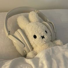 a white teddy bear with headphones laying in bed