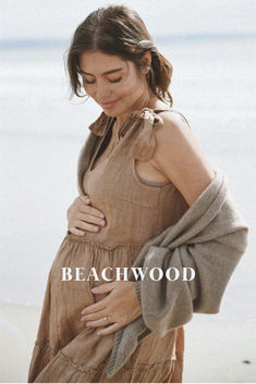 a pregnant woman standing on the beach holding her belly