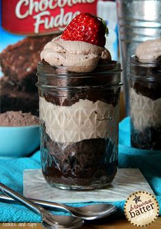 a chocolate dessert in a glass jar with a strawberry on top and some cookies behind it