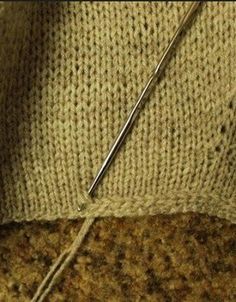 a close up of a knitted sweater with a needle in the middle and yarn on the bottom