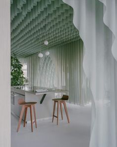 two wooden stools in front of a white kitchen counter with green curtained walls