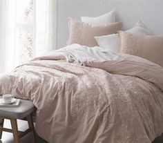 a bed with pink comforters and pillows in a room next to a window,