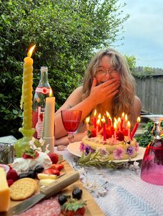 a woman sitting in front of a cake with lit candles on it and surrounded by other foods