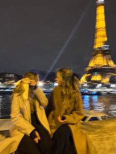 two women sitting next to each other in front of the eiffel tower at night