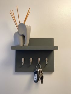 a couple of keys are hanging on a shelf with some hooks and a vase next to it