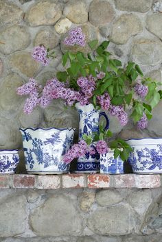 purple flowers are in blue and white vases on a stone ledge next to a brick wall