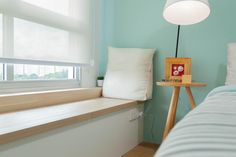 a bed sitting under a window next to a wooden table with a lamp on it