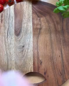 a wooden cutting board sitting on top of a table next to tomatoes and other vegetables