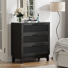 a bedroom scene with focus on the chest of drawers and flowers in front of the window