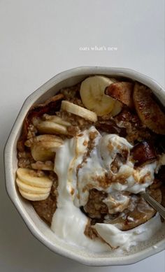 a bowl filled with cereal and bananas on top of a white countertop next to a spoon