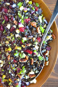 a bowl filled with black rice, nuts and cranberry salad on top of a wooden table