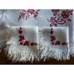 three white towels with red flowers and fringes are on a wooden table next to each other