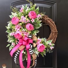 a wreath with pink flowers and greenery is hanging on the front door to welcome guests