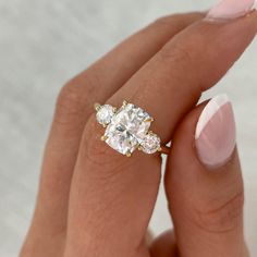 a woman's hand holding an engagement ring with three stones on it and the middle finger