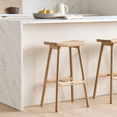 two wooden stools sitting in front of a white counter top next to a bowl of fruit