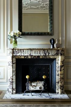 a living room with a fireplace, mirror and flowers on the mantel above it