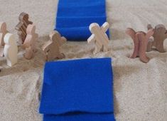 several small wooden people are standing in the sand near a blue towel and some pieces of wood