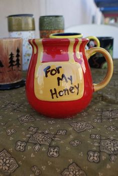 a red and yellow pitcher sitting on top of a table next to two mugs