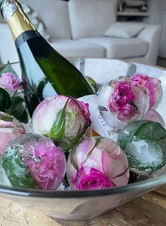 a glass bowl filled with pink flowers next to a bottle of champagne and a white couch