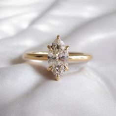 a yellow gold engagement ring with a single diamond on the top and bottom, sitting on a white satin surface