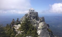 the top of a mountain with a small building on it's side and trees around it