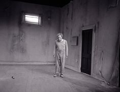 black and white photograph of woman standing in an empty room with no one on the floor