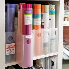 several different colored pens and other office supplies in a white bookcase with clear bins