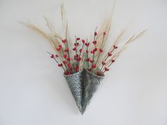 a vase filled with red flowers on top of a white wall next to dry grass