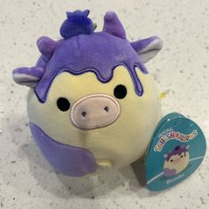 a stuffed animal with purple hair and nose sitting next to a tag on the floor