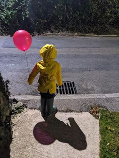 a person in a yellow raincoat holding a pink balloon