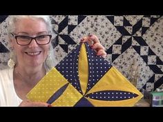 a woman holding up a yellow and blue quilt