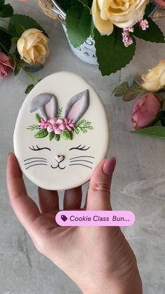 a hand holding up a cookie with an image of a bunny on it and flowers in the background