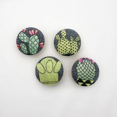 four cactus buttons on a white surface with green and pink flowers in the center, three are made out of fabric