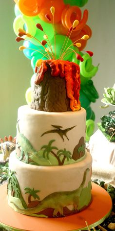 a three tiered cake is decorated with dinosaurs and palm trees on the bottom layer