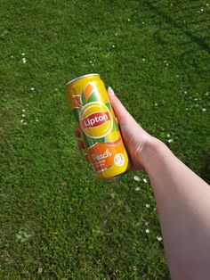 a person holding up a can of orange juice in their hand on the grass outside