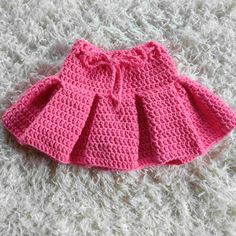 a pink crocheted skirt is laying on a white carpet and it has a bow at the waist