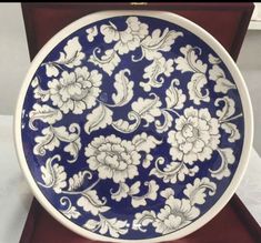 a blue and white plate with flowers on it sitting in a wooden box for display