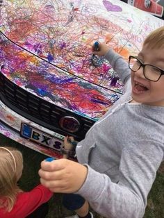 two young children are painting on the hood of a car with colorful paint splattered all over it