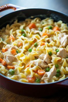 a pan filled with chicken noodle and carrots on top of a wooden table