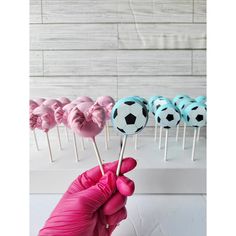 a hand is holding several lollipops with soccer balls on them in pink gloves