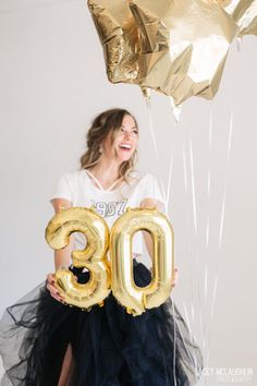 a woman holding two balloons and the number eighteen in front of her is wearing a tutu skirt