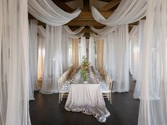 a long table is set up with white drapes on the ceiling and chairs around it