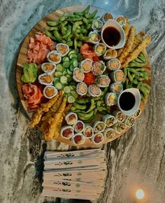 an assortment of sushi on a wooden platter with chopsticks and dipping sauce