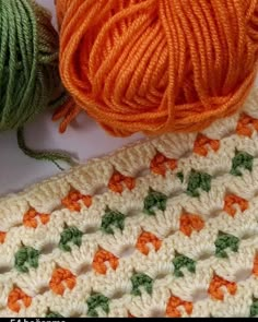 two balls of yarn sit next to each other on a white surface with orange and green crochet