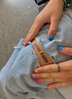 a woman's hands with colorful nail polishes on her nails holding onto a ripped piece of denim